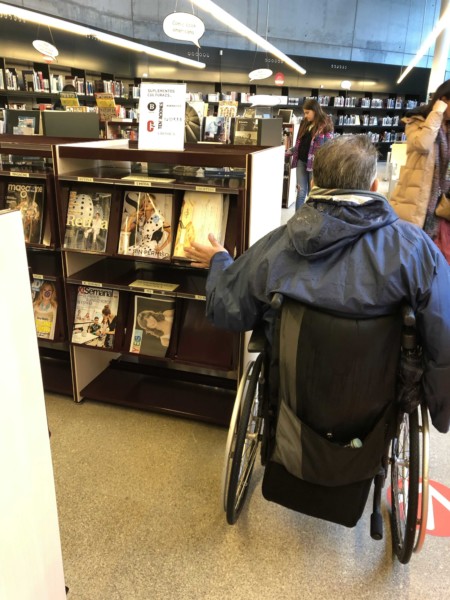 mobiliario accesible Usuario en silla de ruedas haciendo uso de un mueble de revistas a una altura correcta