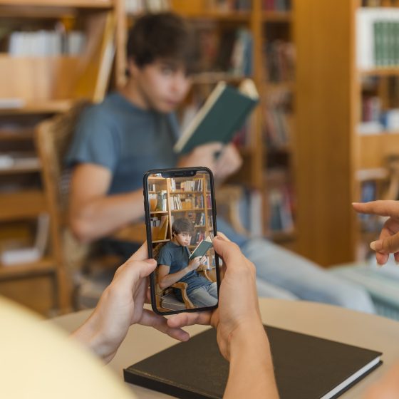 Adolescente leyendo un libro en una biblioteca mientras lo graban con un móvil