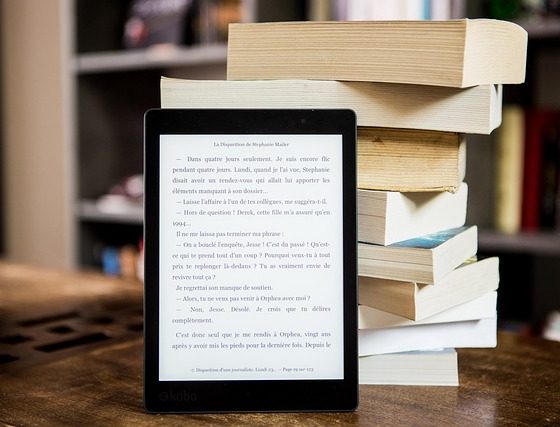 lector de libro electrónico en el primer plano. Está apoyado en un montón de libros en papel